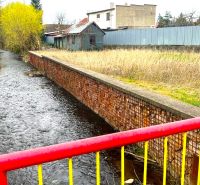 Rovinatý stavebný pozemok - Šaca - Obrázok z Jarkovej ulice, Košice - mestská časť Šaca, s riečkou a priľahlými pozemkami.