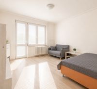 Na prenájom zariadený 4-izbový byt s balkónom I Ružinov |  - Svetlá izba so sedačkou, posteľou a podlahou s dreveným dekorom v 4-izbovom byte.