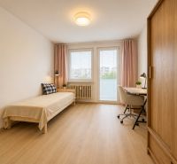 Pekný zariadený 3-izbový byt s 2 balkónmi | 85,3 m² | Petržalka I - Izba v 3-izbovom byte s posteľou, stolom a podlahou s dreveným dekorom.
