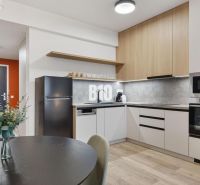 DOWNTOWN NA DOSAH – DIZAJNOVÝ 1-izbový apartmán s loggiou a výhľadom n - Kuchyňa s jedálenským stolom, spotrebičmi a podlahou s dreveným dekorom v 1-izbovom byte.