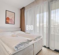 DOWNTOWN NA DOSAH – DIZAJNOVÝ 1-izbový apartmán s loggiou a výhľadom n - Spálňa s posteľou, nočným stolíkom, obrazom a priesvitnými závesmi v 1-izbovom byte.
