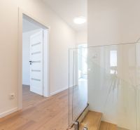 NOVOSTAVBA- NÍZKOENERGETICKÝ4 IZB.RODINNÝ DOM- LORINČÍK HÁJE-PREDAJ-KE - Interiér rodinného domu s podlahou s dreveným dekorom a skleneným zábradlím pri schodoch.