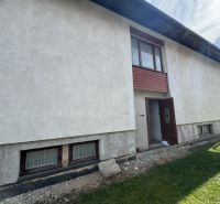 Rozostavaný rodinný dom Plavnica - Rodinný dom v Plavnici so svetlou omietkou a drevenými oknami na prízemí.
