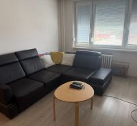 2,5 izbový byt v centre Lučenca - Obývacia izba v 2-izbovom byte s čiernym gaučom a podlahou s dreveným dekorom.