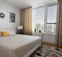 PENTHOUSE – moderný 2i byt s výnimočnou 69 m² terasou, AHOJ PARK - Spálňa v 2-izbovom byte s veľkým oknom, posteľou a dekoračnou podlahou s dreveným dekorom.