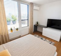 PENTHOUSE – moderný 2i byt s výnimočnou 69 m² terasou, AHOJ PARK - Svetlá spálňa s posteľou, televízorom a podlahou s dreveným dekorom v 2-izbovom byte.