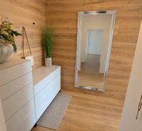 PENTHOUSE – moderný 2i byt s výnimočnou 69 m² terasou, AHOJ PARK - Interiér 2-izbového bytu s bielou komodou, zrkadlom a podlahou s dreveným dekorom.