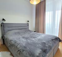 ŠTÝLOVÝ 2i byt, PARKING, KLÍMA, PARKING, Čulenova ulica, SKY PARK - Spálňa s posteľou, nočným stolíkom, závesmi a podlahou s dreveným dekorom v 2-izbovom byte.