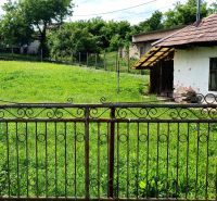 NA PREDAJ stavebný pozemok  v Plavých Vozokanoch - Starší dom s plotom na pozemku, obklopený zeleňou, ideálny pre bývanie.