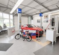 MODERNÝ, ZABEHNUTÝ, KOMPLETNE ZARIADENÝ AUTOSERVIS, LOZORNO - Interiér výrobných priestorov s autom, bicyklom a kreslami, podlaha s dlaždicami.