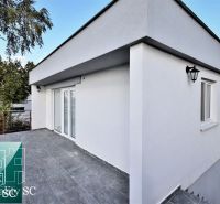 SENEC – SLNEČNÉ JAZERÁ JUH – NA PREDAJ - romantická rekreačná chata s  - Terasa pri chate v Senci na SLNEČNÝCH JAZERÁCH JUH s bielou fasádou a stromami.
