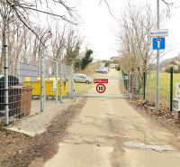 Na predaj stavebný pozemok Koliba, Sovia ulica - Brána na ulici Na Vtáčniku, vedľa smetných kontajnerov, obklopená stromami a pozemkami na bývanie.