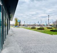 Na PREDAJ | nebytový priestor | Prístavná ulica - Obchodné priestory na Prístavnej ulici, Bratislava - Ružinov s kvetinovými záhonmi a dlažbou.