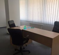 Kancelárie v centre mesta. - Jednoduchá kancelária s dreveným stolom, dvoma stoličkami a žalúziami na oknách.