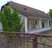Vidiecky domček na predaj. - Rodinný dom v Ňárade so šikmou strechou, stĺpmi a viditeľným plotom, obklopený zeleňou.