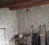 Vidiecky domček na predaj. - Interiér rodinného domu s tehlovými stenami, stoličkou a dvoma fúrikmi.