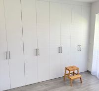 Luxusný byt na prenájom. - Biely vstavaný šatník s dreveným dekorom a stoličkou v 2-izbovom byte.