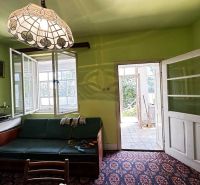 Na predaj starší rodinný dom vhodný na kompletnú prestavbu s  veľkým p - Svetlo zelená stena, sedacia súprava, vintage lampa a otvorené dvere v rodinnom dome.