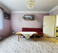 Na predaj starší rodinný dom vhodný na kompletnú prestavbu s  veľkým p - Obývacia izba v rodinnom dome s červenou sedačkou a dekoratívnymi tapetami.