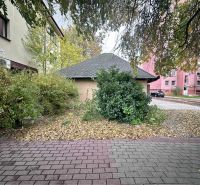 Znížená cena     Predaj – Obchodný priestor v Dunajskej Strede 100 000 - Zeleň obklopujúca obchodné priestory v Dunajskej Strede s chodníkom a budovami v pozadí.