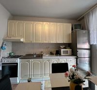 Na predaj kompletne zariadený 3 izbový byt s klimatizáciou aj s balkón - Kuchyňa v 3-izbovom byte s krémovými skrinkami, spotrebičmi a prestretým stolom.