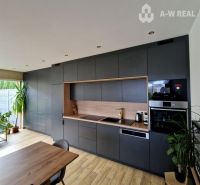 Znížená cena    Luxusný 4-izbový rodinný dom s letnou kuchyňou a nádhe - Kuchyňa v rodinnom dome s podlahou s dreveným dekorom a šedými skrinkami.