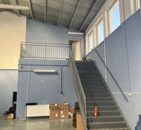 Prenájom skladový priestor v centre mesta + vlastné parkovanie - Sklady a haly s kovovým schodiskom, krabicami a pneumatikami na podlahe.