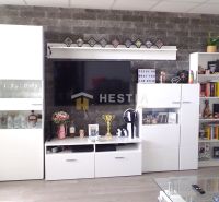 Moderný 3-izbový byt s lodžiou po rekonštrukcii - Obývacia izba s bielymi skrinkami a televízorom, podlaha s dreveným dekorom.
