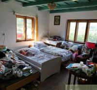 Veľký, vyše 4,5Ha slnečný pozemok s chalupou v strede, na lazoch, pri  - Chata s posteľou, oknami, podlahou s dreveným dekorom a rôznymi vecami na stoloch.