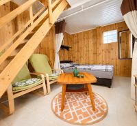 INVESTIČNÁ PRÍLEŽITOSŤ V SRDCI ŠTÚROVA - ZABEHNUTÉ APARTMÁNY - Rodinný dom s dreveným obkladom, zelenými kreslami a posteľou v interiéri.
