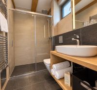 Predaj! INVESTUJTE DO MIESTA, KAM SA ĽUDIA VRACAJÚ – TATRALANDIA - Moderná kúpeľňa so sprchovacím kútom a podlahou s dreveným dekorom v rodinnom dome.