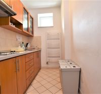 Prenájom kancelárskych priestorov, 56 m2 – Ružinov, Bratislava - Kancelárie s kuchynkou, drevený dekor, tri odpadkové koše, úzke okno na stene.