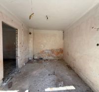 Rodinný dom v centre obce s potokom priamo za domom - Izba v rodinnom dome pred rekonštrukciou s odkrytými stenami a podlahou.