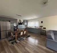 ** NOVOSTAVBA S KRBOM ** 4 izb. RD, ÚP 130m2, pozemok 584m2 – FIGOVÁ - Otvorená kuchyňa s jedálenským stolom a podlahou s dreveným dekorom v rodinnom dome.