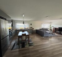 ** NOVOSTAVBA S KRBOM ** 4 izb. RD, ÚP 130m2, pozemok 584m2 – FIGOVÁ - Otvorený interiér rodinného domu s kuchyňou, jedálenským stolom, pohovkou a podlahou s dreveným dekorom.