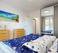 PRENÁJOM 2 izbový, zariadený byt v Danube residencia - REZERVOVANÉ - Spálňa v 2-izbovom byte s podlahou s dreveným dekorom, bielymi stenami a obrazom pláže.