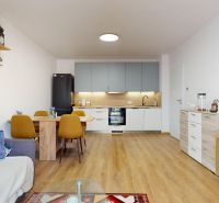 PRENÁJOM 2 izbový, zariadený byt v Danube residencia - REZERVOVANÉ - Obývačka s kuchyňou v 2-izbovom byte s podlahou s dreveným dekorom a jedálenským stolom.
