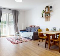 PRENÁJOM 2 izbový, zariadený byt v Danube residencia - REZERVOVANÉ - Obývacia izba s pohovkou, jedálenským stolom a podlahou s dreveným dekorom v 2-izbovom byte.