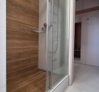 Moderne vybavený a zariadený 1-izbový byt s balkónom na sídlisku JUH - Sprchový kút s dreveným dekorom v 1-izbovom byte s bielou dlažbou.