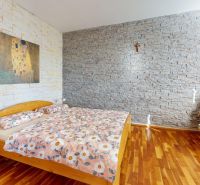 PREDAJ - 4-izb. byt v bytovke, Hamuliakovo, 115 m2 + balkón, výťah - Spálňa s kamennými stenami, posteľou a kreslom, podlaha s dreveným dekorom.
