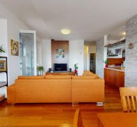 PREDAJ - 4-izb. byt v bytovke, Hamuliakovo, 115 m2 + balkón, výťah - Obývacia izba so svetlými prvkami, koženou sedačkou a podlahou s dreveným dekorom.
