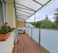 Pekný 3-izbový byt s balkónom na prenájom - Balkón v 3-izbovom byte s podlahou s dreveným dekorom, kvetmi a výhľadom.