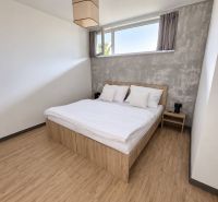 ViBee Liptov:apartmán s odhadom 5 % hrubého výnosu a vlastnými pobytmi - Spálňa v 2-izbovom byte s posteľou, sivou stenou a podlahou s dreveným dekorom.