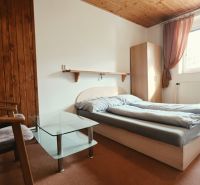 Na predaj zabehnutý Apartmánový dom v Podhájskej s parkovaním - Spálňa Rekreačného apartmánu s manželskou posteľou, kreslami a oknom, podlaha s dreveným dekorom.