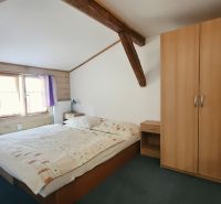 Na predaj zabehnutý Apartmánový dom v Podhájskej s parkovaním - Spálňa v Rekreačnom apartmáne s drevenými trámami, skriňou a posteľou vedľa okna.