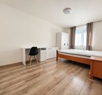 PRENÁJOM | Moderný 2-izbový byt s balkónom a parkovaním – SL - Izba v 2-izbovom byte s posteľou, stolom a podlahou s dreveným dekorom.