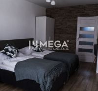 Na predaj nehnuteľnosť - zabehnutý penzión v centre mesta Humenné - Interiér izby s dvomi posteľami, stena s dekorom kameňa, podlaha s dreveným dekorom.
