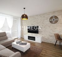 NA PRENÁJOM – PRÉMIOVÝ 3-IZBOVÝ BYT S PANORAMATICKÝM VÝHĽADOM - Obývacia izba so svetlou sedačkou a podlahou s dreveným dekorom v 3-izbovom byte.
