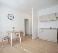 REZERVOVANÉ 1 izbový byt s balkónom - až 41m² N. DUBNICA - Kuchyňa v 1-izbovom byte s podlahou s dreveným dekorom, jedálenským stolom a hodinami.