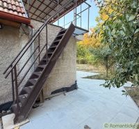 Záhrada s murovanou chatkou po rekonštrukcii iba 200 m od rieky Nitra - Exteriér chaty v Nových Zámkoch s kovovým schodiskom a terasou obklopenou zeleňou.